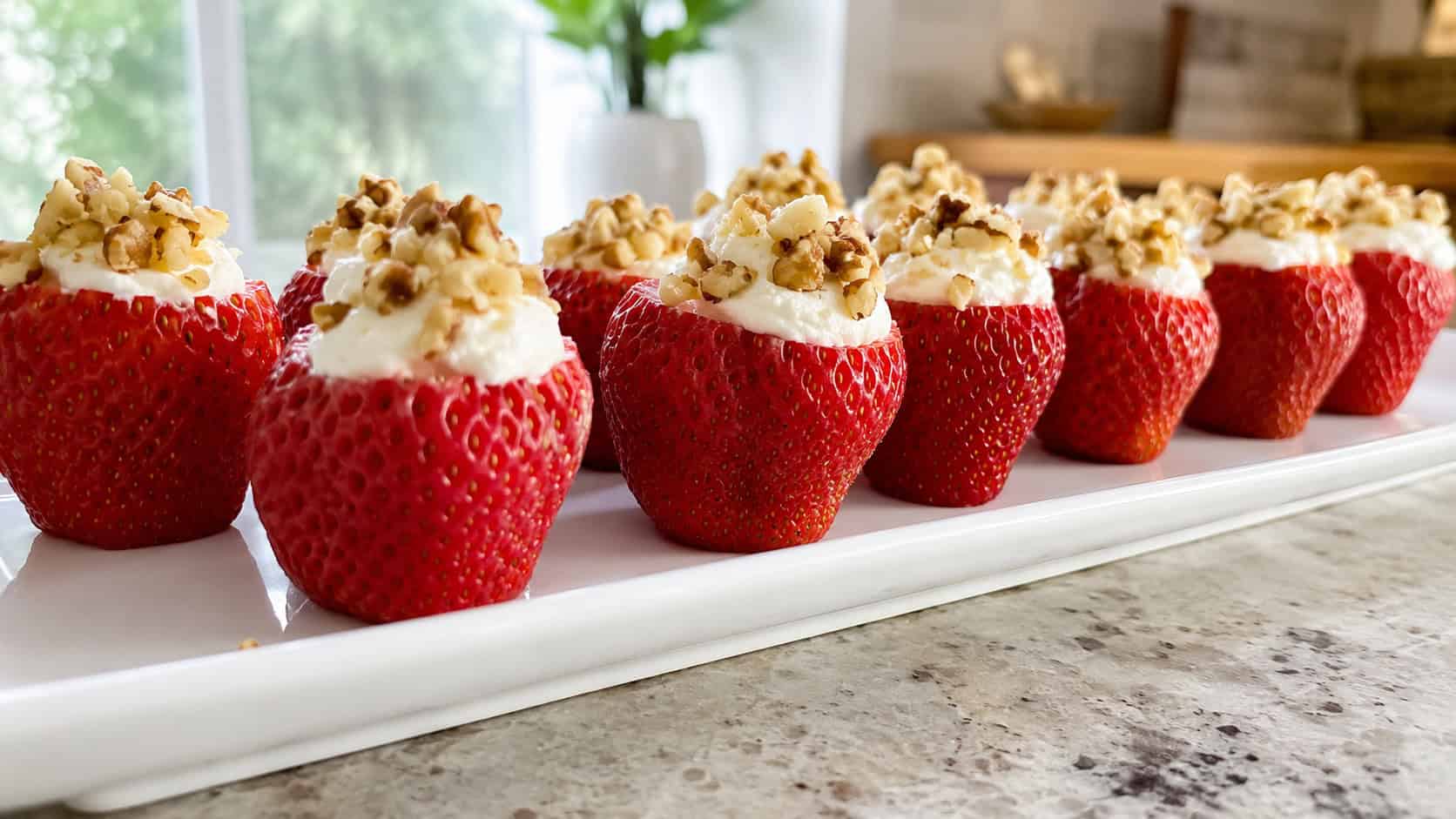 stuffed strawberries filled with creamy white filling and topped with chopped walnuts, arranged in a wide horizontal row on a white platter, bright natural light, shallow depth of field, landscape orientation