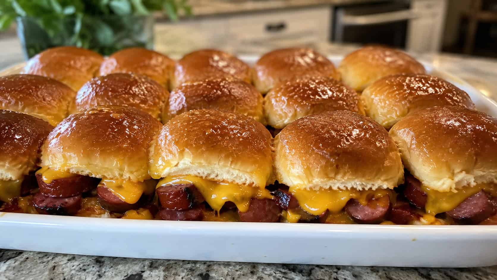 barbecue smoked sausage sliders on soft golden buns with melted cheddar lined up in a baking dish, in a wide horizontal shot, glossy buttered tops, on a kitchen counter, natural light, shallow depth of field, landscape orientation