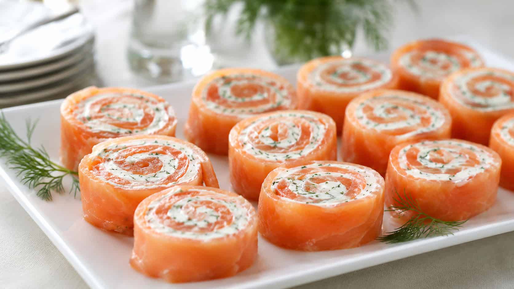 smoked salmon pinwheels with pink salmon and creamy swirls flecked with dill arranged on a white platter, in a wide horizontal shot on a bright table, natural light, shallow depth of field, landscape orientation