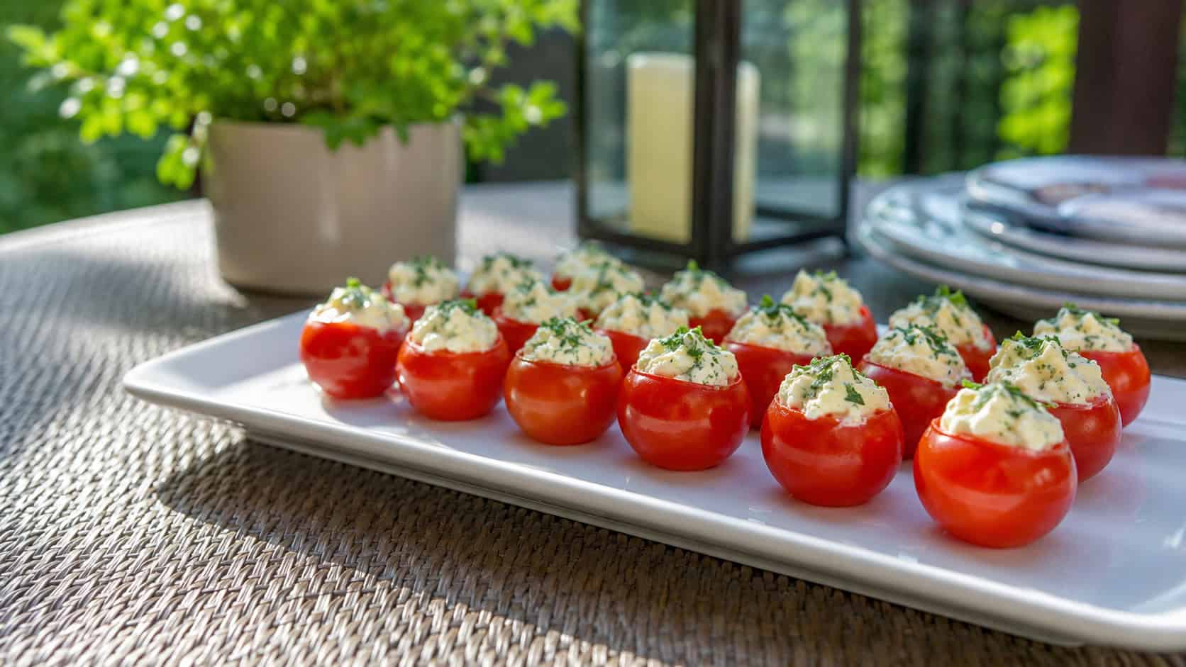 bright red cherry tomatoes filled with creamy herb-flecked filling arranged on a platter, in a wide horizontal shot on a sunny patio table, natural light, shallow depth of field, landscape orientation