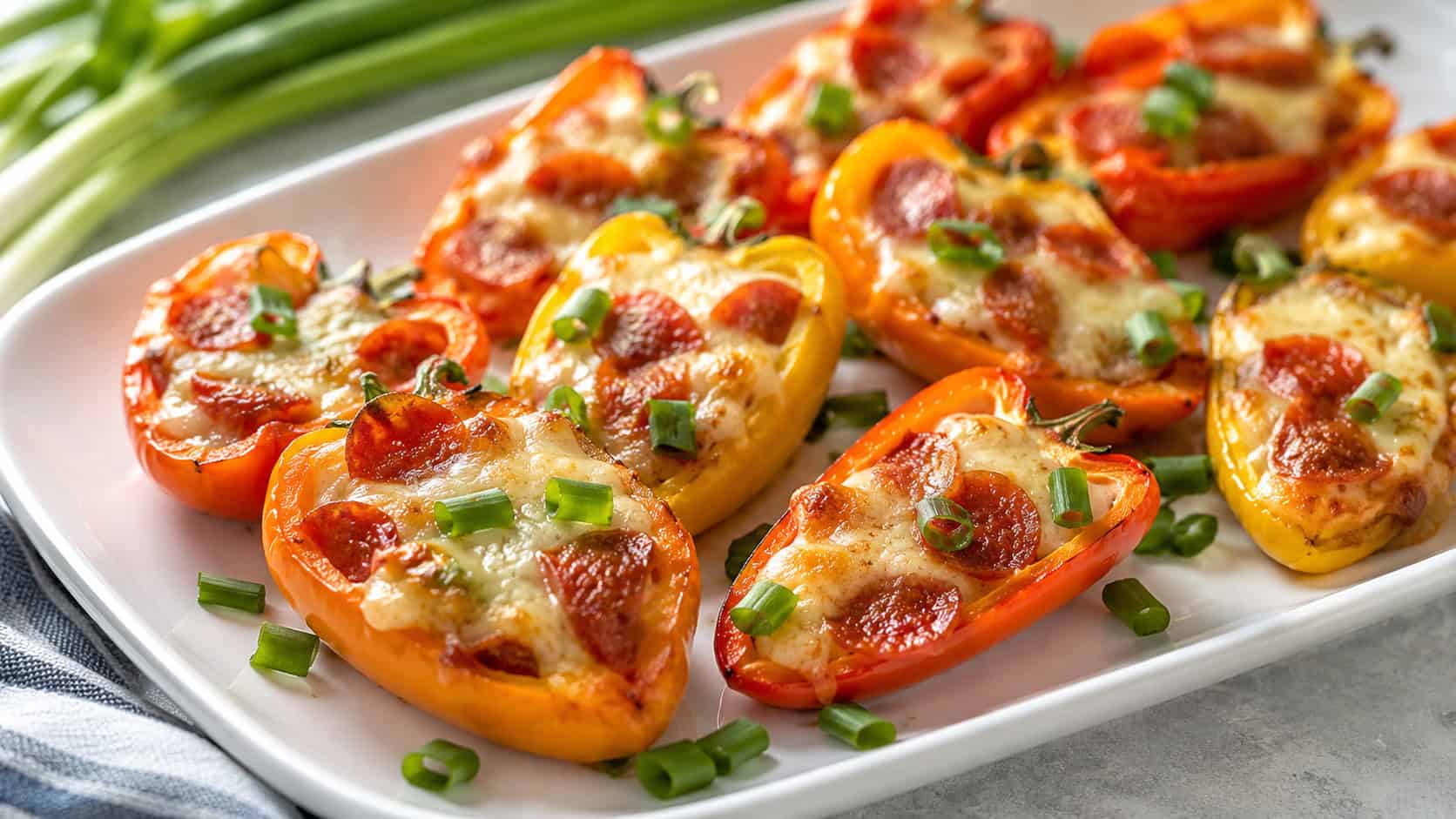 colorful mini sweet peppers stuffed with melted pepperoni cheese filling on a platter in a wide horizontal shot, on a bright table with green onion garnish, fresh natural light, shallow depth of field, landscape orientation