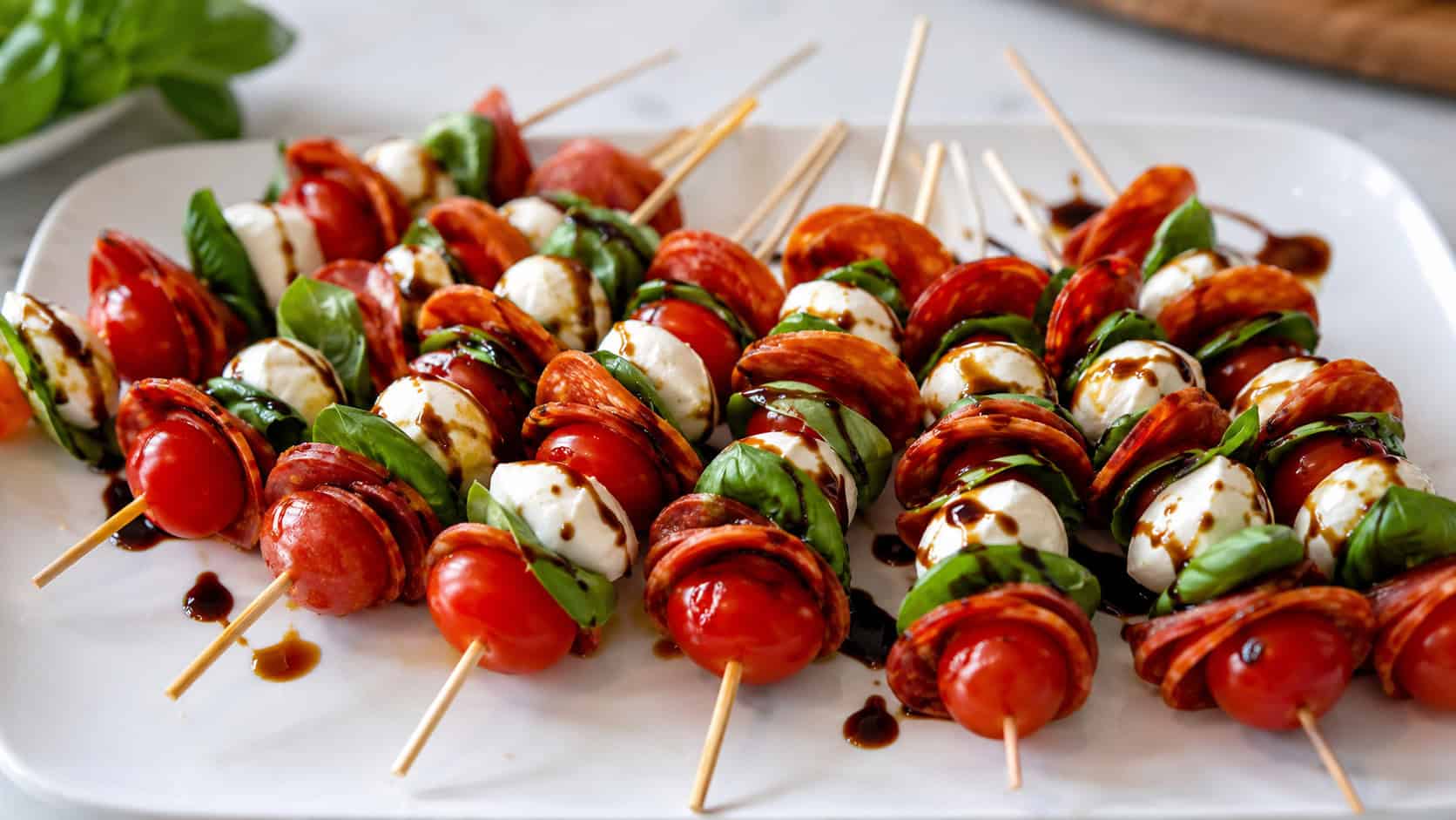 colorful skewers of pepperoni, mozzarella, tomato, and basil with balsamic drizzle in a wide horizontal shot, fanned out on a white platter, fresh bright light, shallow depth of field, landscape orientation