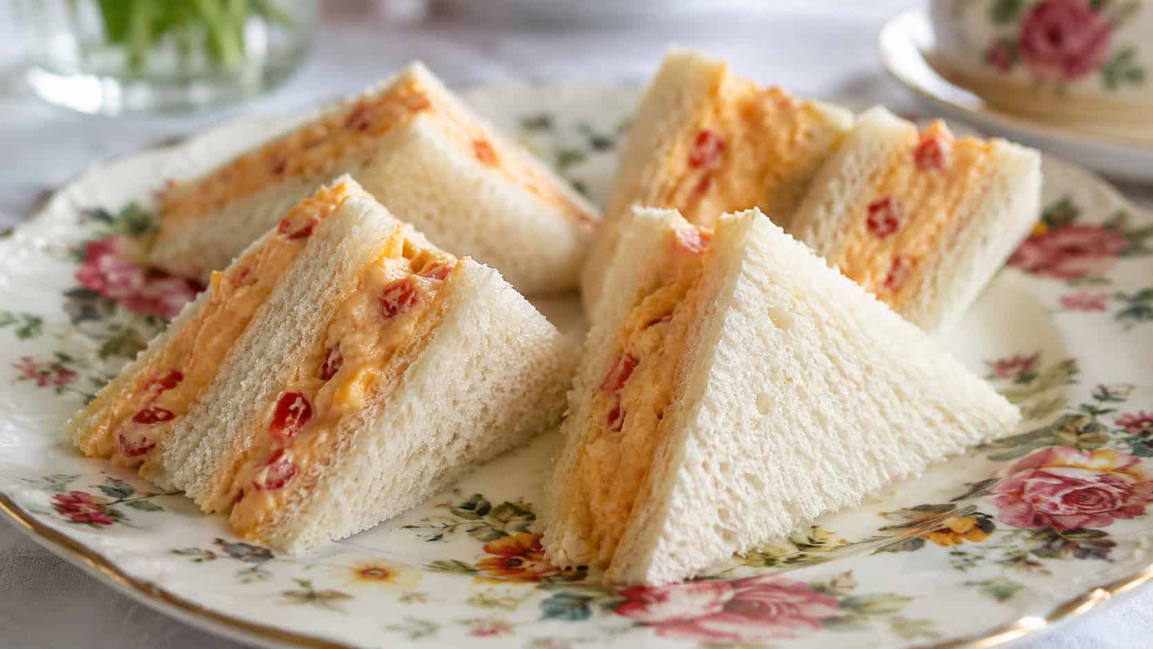 pimento cheese tea sandwiches cut into triangles showing the creamy orange filling, arranged on a vintage floral plate, in a wide horizontal shot, bright natural light, shallow depth of field, landscape orientation