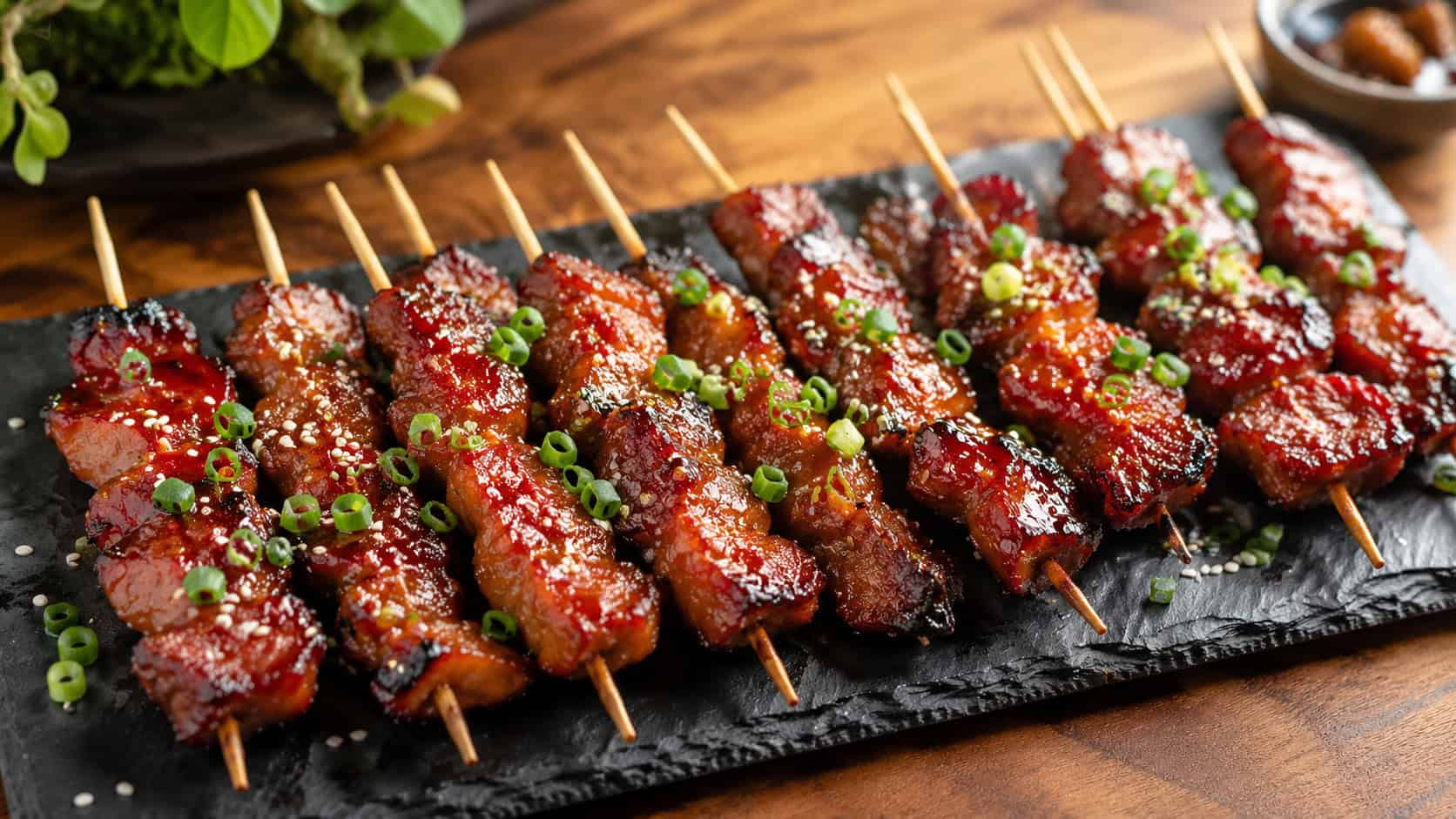 a wide horizontal platter of glossy red char siu pork skewers with caramelized charred edges, sprinkled with sesame seeds and scallion, on a slate board, warm natural light, shallow depth of field, landscape orientation
