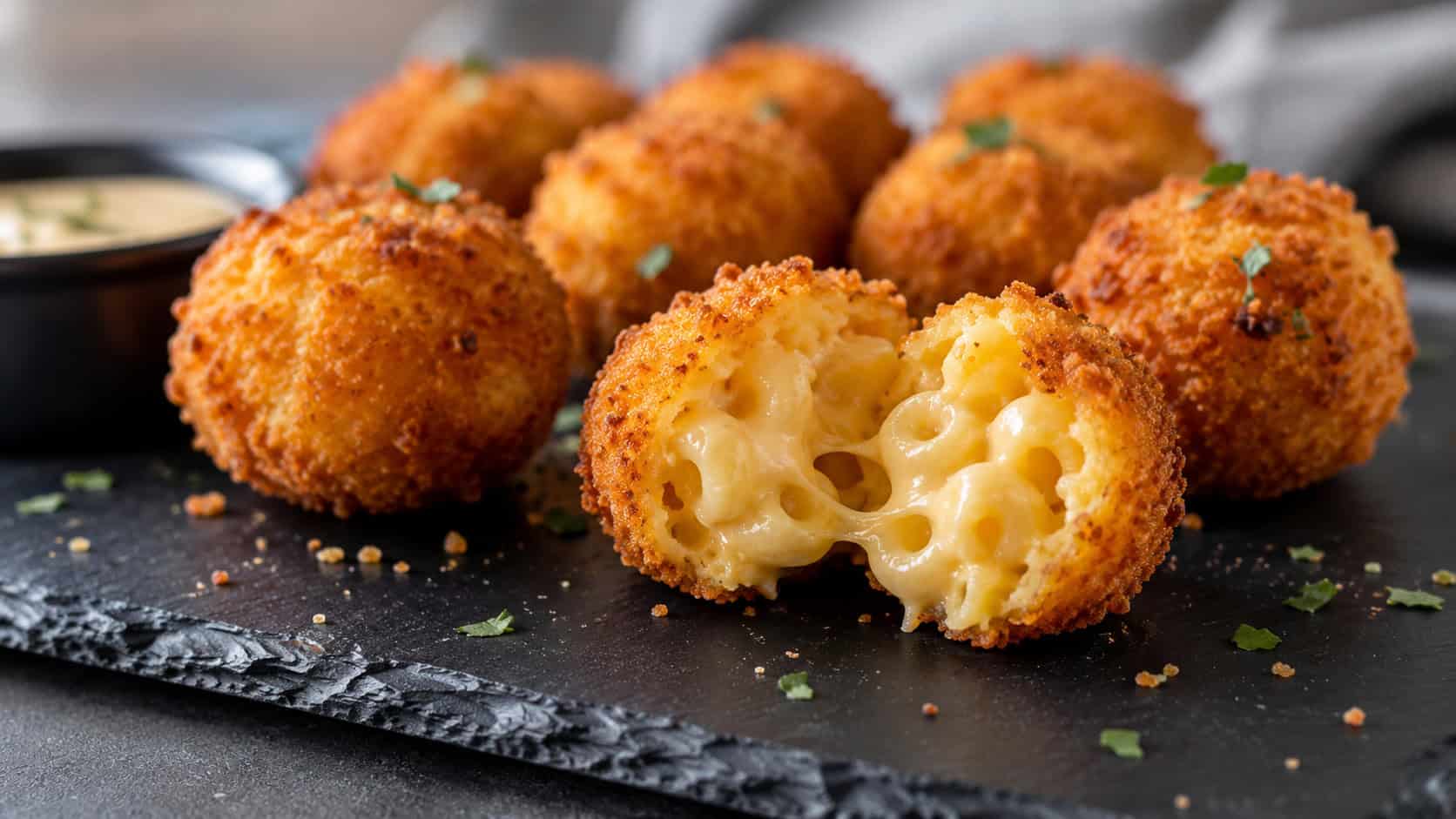 golden fried mac and cheese bites in a wide horizontal shot, one broken open to show creamy cheese on a slate board, natural light, shallow depth of field, landscape orientation