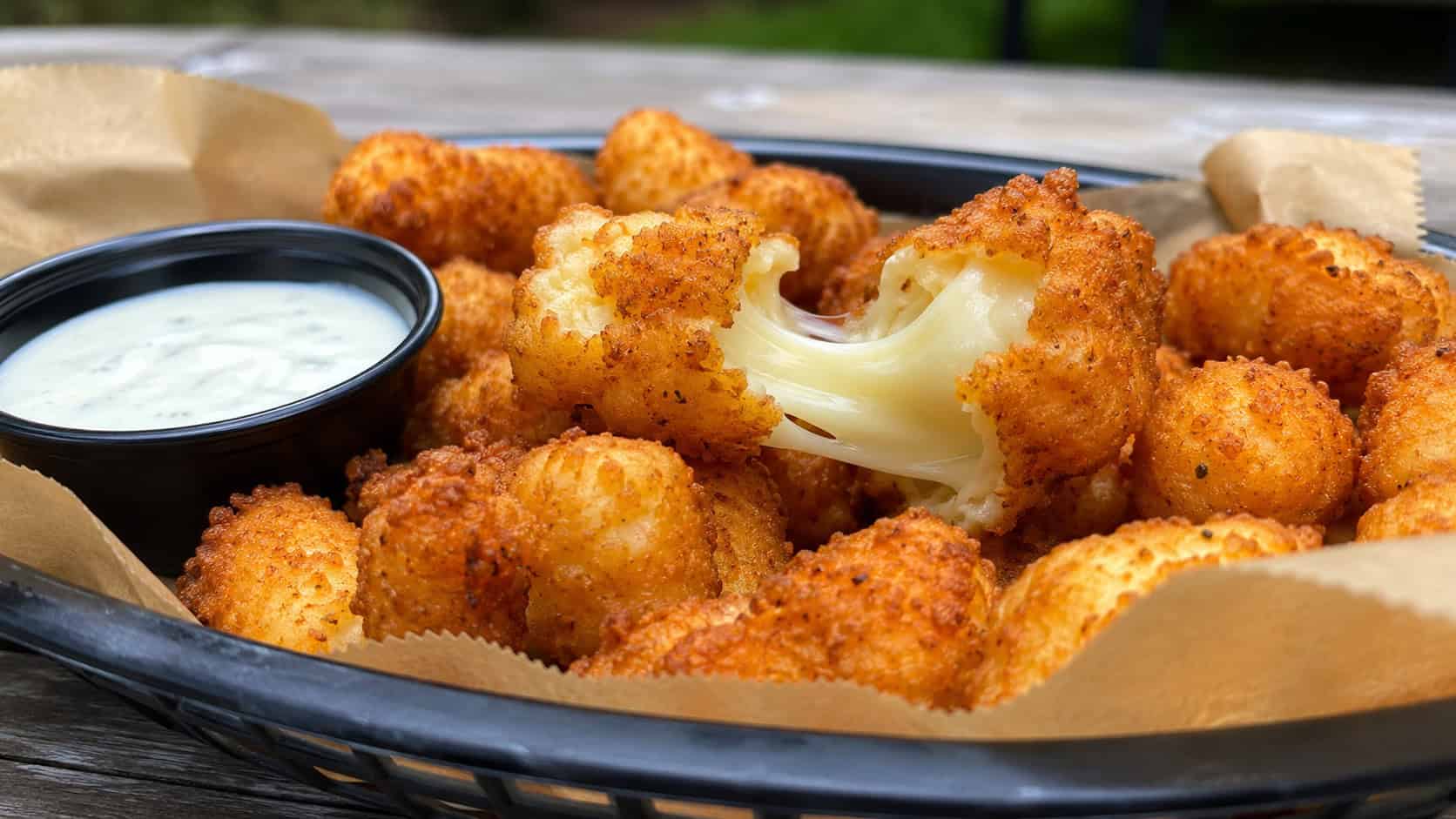 golden fried cheese curds in a wide horizontal shot, one pulled open to show melted cheese in a basket with ranch, natural light, shallow depth of field, landscape orientation