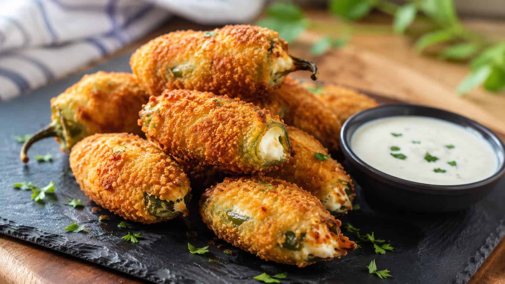 crispy fried jalapeño poppers in a wide horizontal shot, golden bites stacked on a slate board with a bowl of ranch, natural light, shallow depth of field, landscape orientation