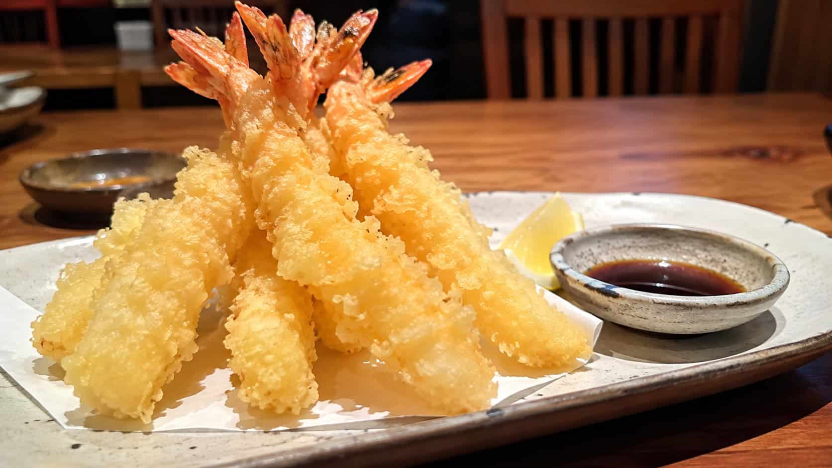 crispy shrimp tempura in a wide horizontal shot, arranged on a plate with a small dish of dipping sauce and lemon, natural light, shallow depth of field, landscape orientation