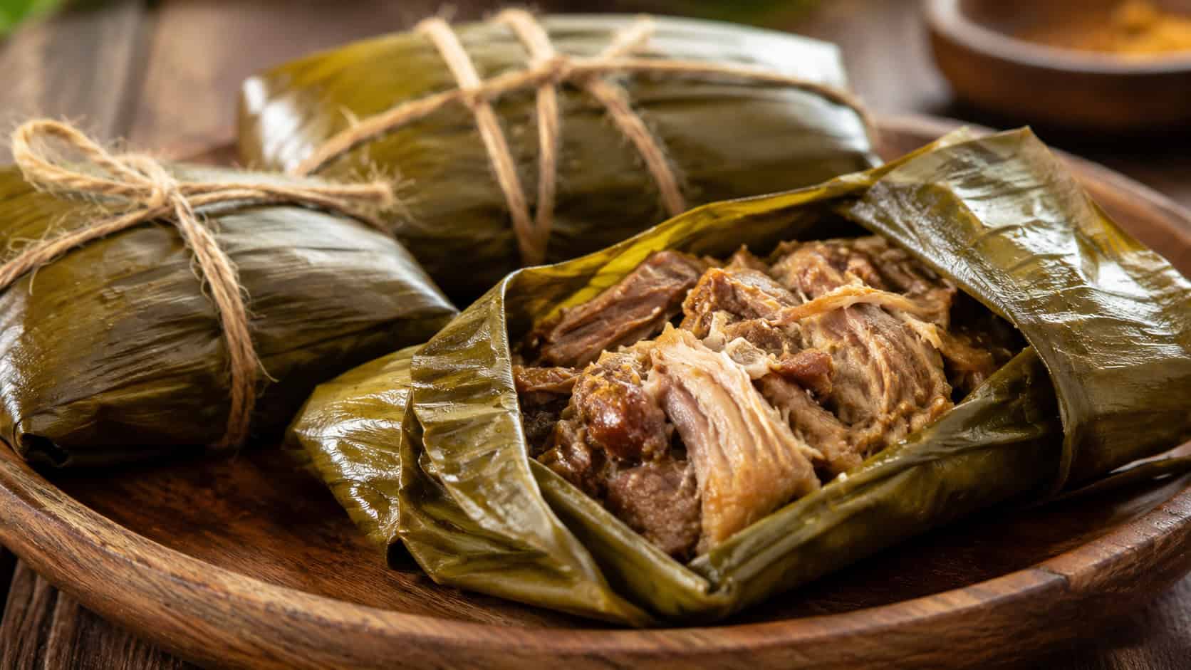 banana leaf wrapped pork bundles, one opened to show tender shredded pork, in a wide horizontal shot, on a rustic wooden platter with twine, warm natural light, shallow depth of field, landscape orientation