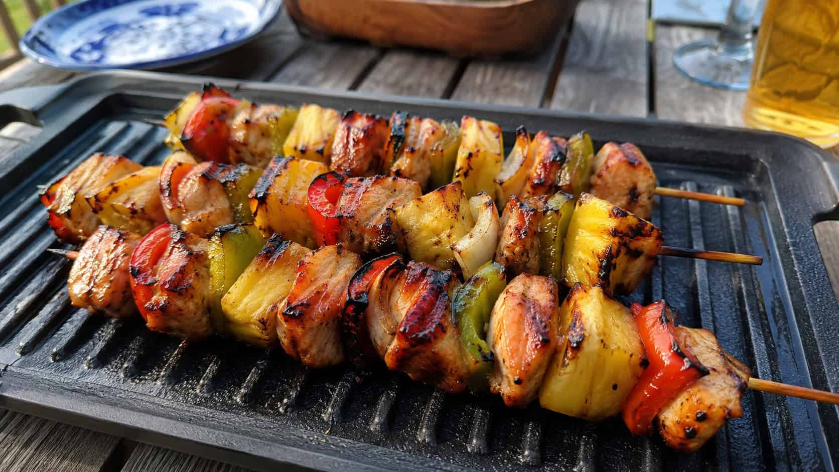 Hawaiian chicken kabobs on a grill platter, in a wide horizontal shot, charred chicken with pineapple and peppers, glossy glaze, on an outdoor table, warm natural light, shallow depth of field, landscape orientation