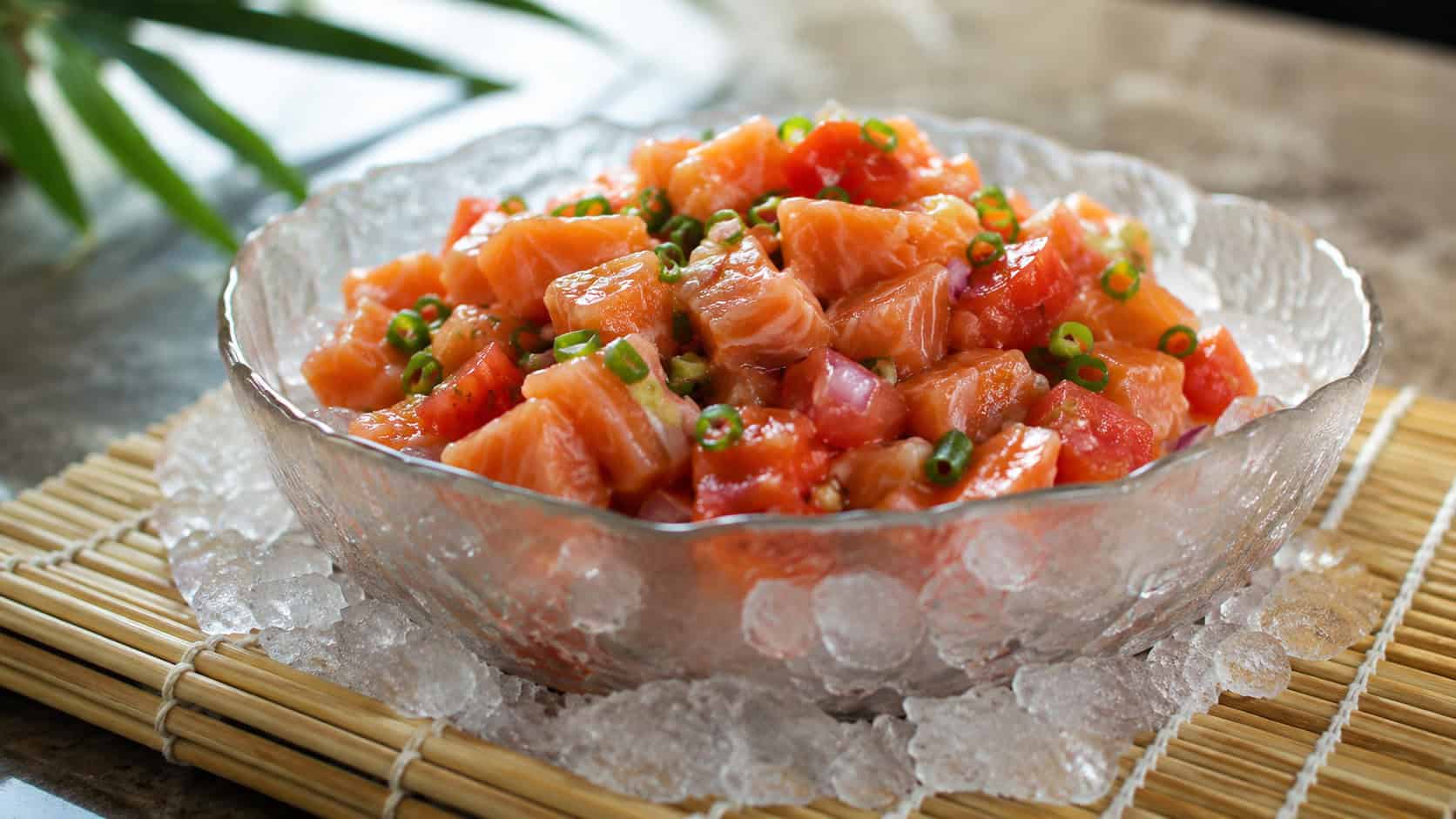 lomi lomi salmon in a chilled bowl, in a wide horizontal shot, diced salmon with tomatoes and green onion, on a bed of ice, on a bamboo mat, cool natural light, shallow depth of field, landscape orientation