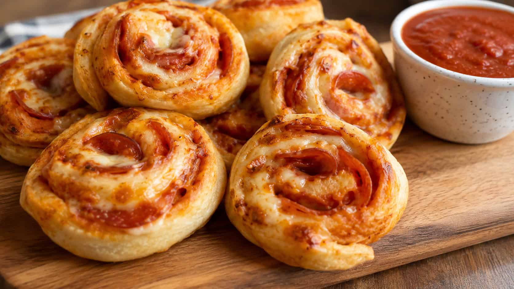 golden pepperoni pizza pinwheel rolls showing swirls of cheese and pepper, arranged on a board with a cup of marinara, in a wide horizontal shot, warm natural light, shallow depth of field, landscape orientation