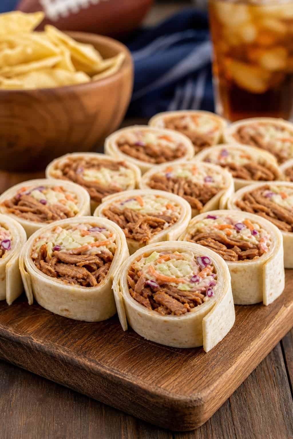Plate of BBQ pulled pork and coleslaw pinwheel appetizers showing dark smoky pulled pork and pale shredded coleslaw inside sliced flour tortilla rolls on a wooden serving board.