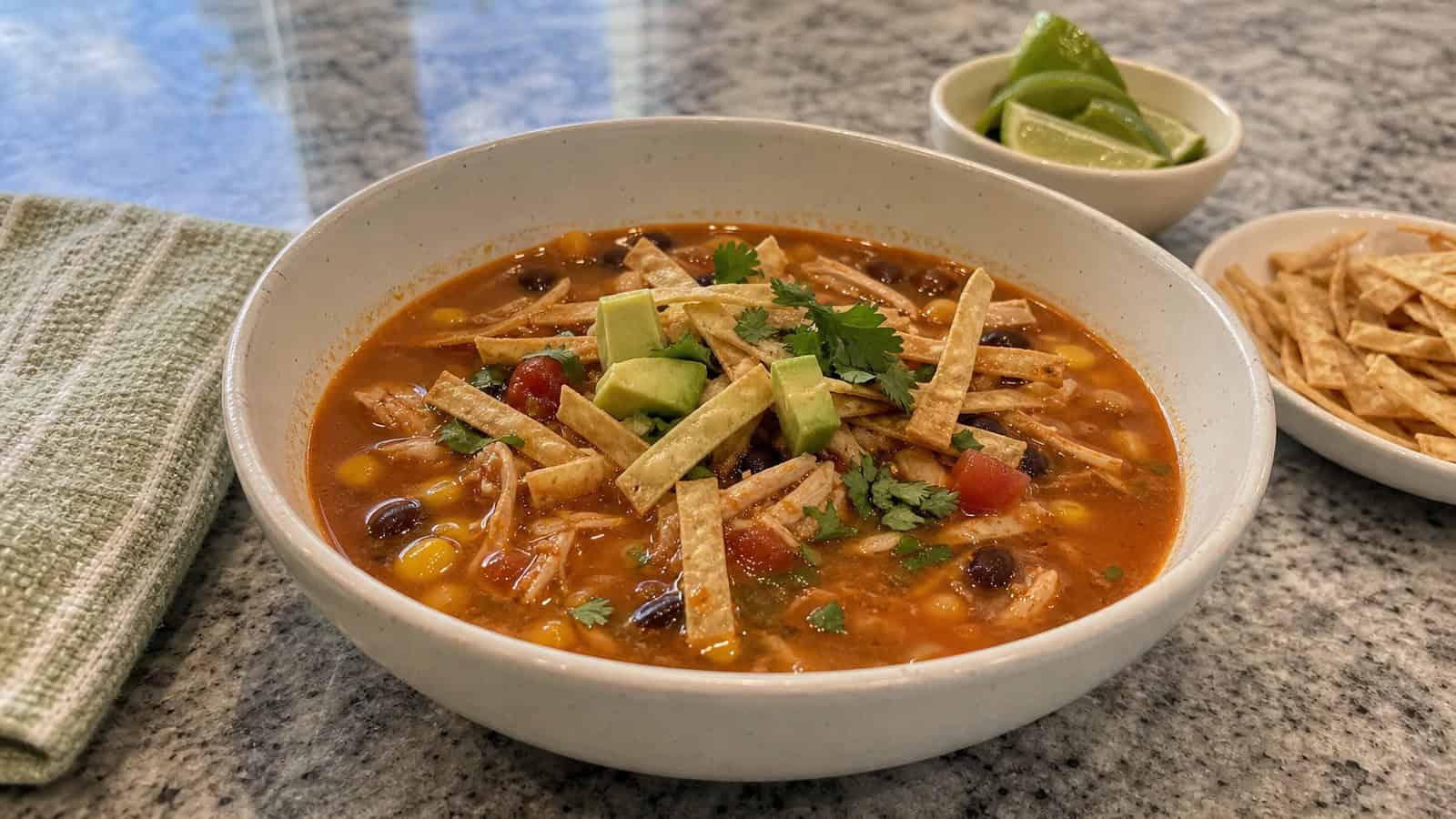 homemade chicken tortilla soup in a bowl with tortilla strips and lime on the side