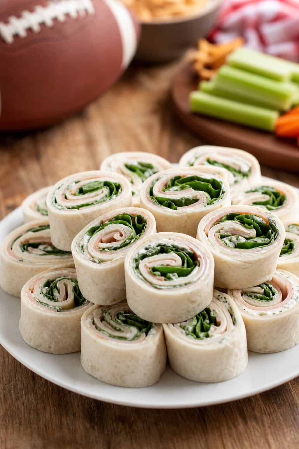 A plate of turkey ranch pinwheel appetizers showing visible layers of green spinach, shredded cheddar, and deli turkey inside sliced flour tortilla rolls.