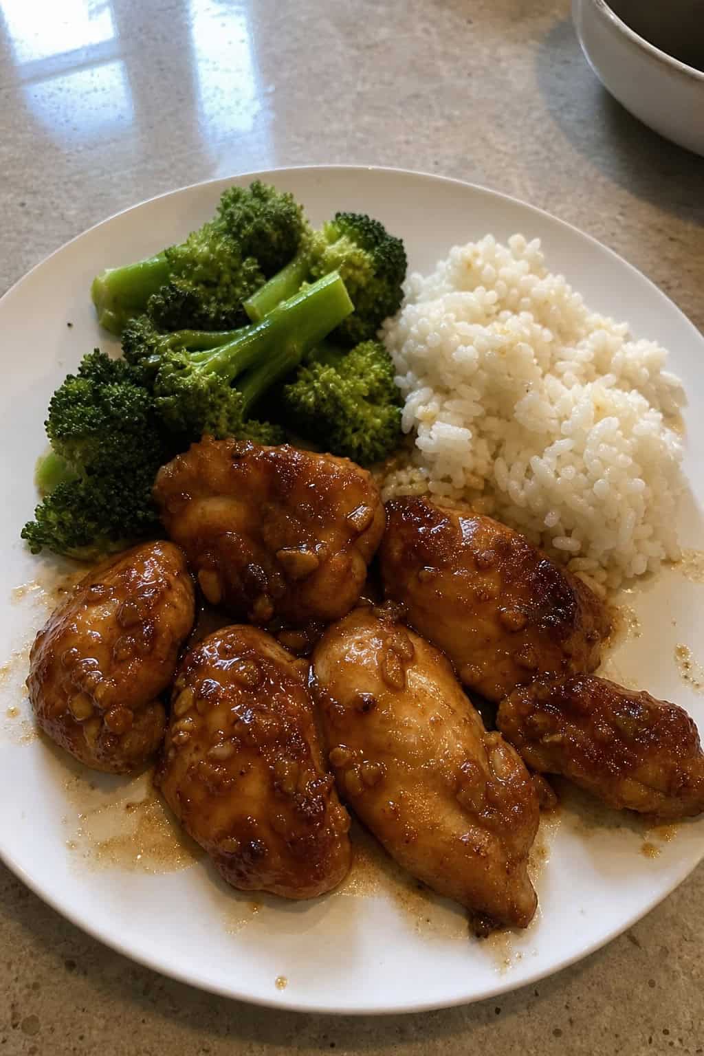 Glazed honey garlic chicken thighs on a white plate, topped with chopped parsley, served alongside steamed vegetables and a mound of white rice.