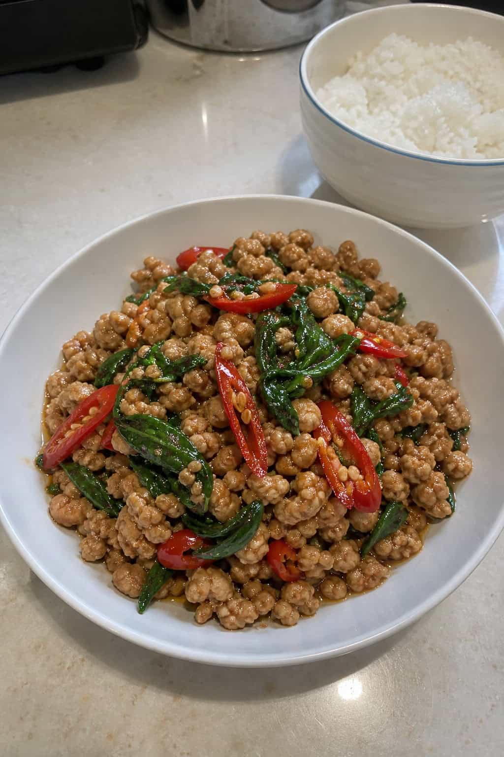 Close-up of a bowl of Thai basil minced chicken stir-fry with fresh herbs and chili on a wooden table.