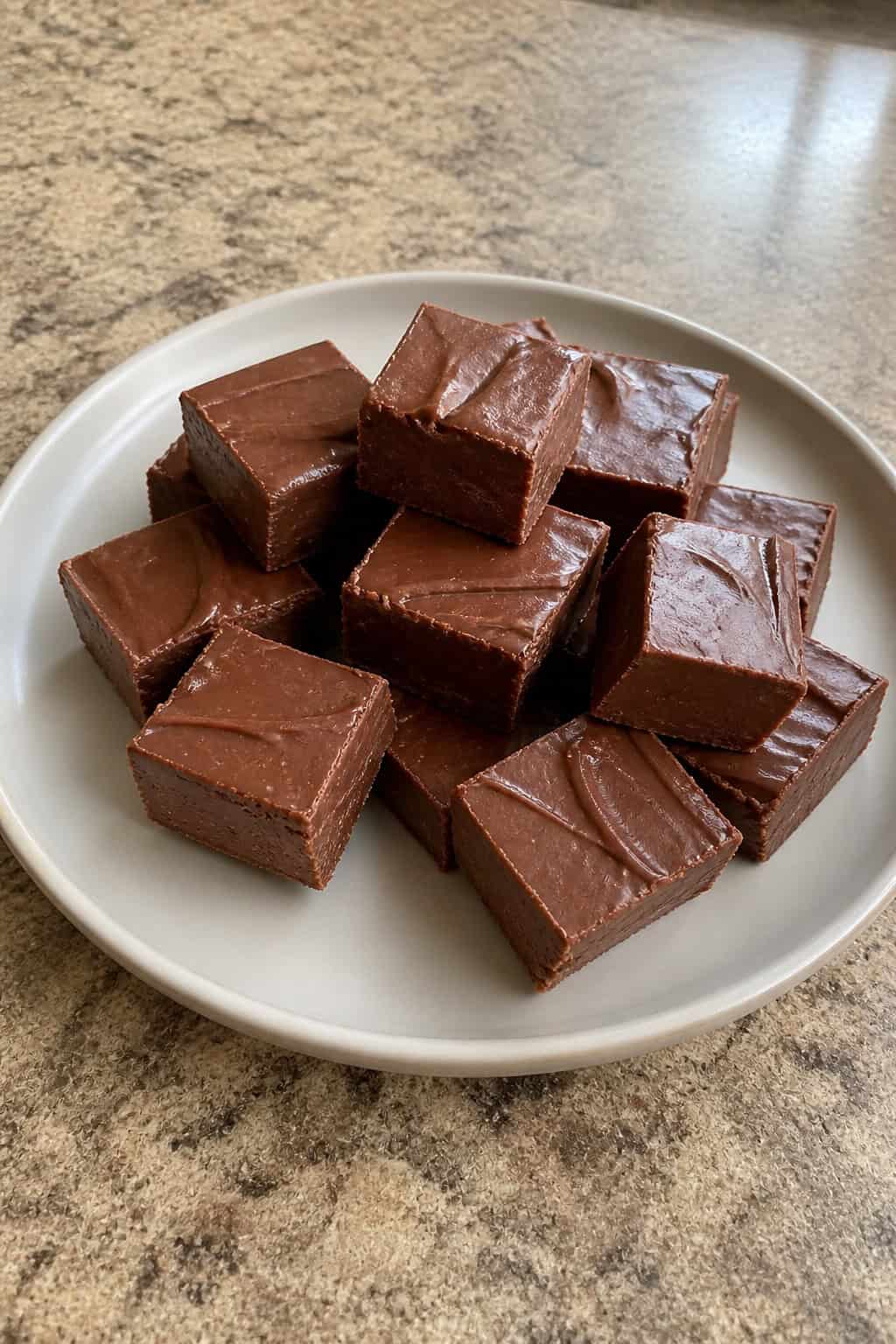 Close-up of several Nutella fudge squares on a white plate with hazelnuts scattered around on a wooden table.