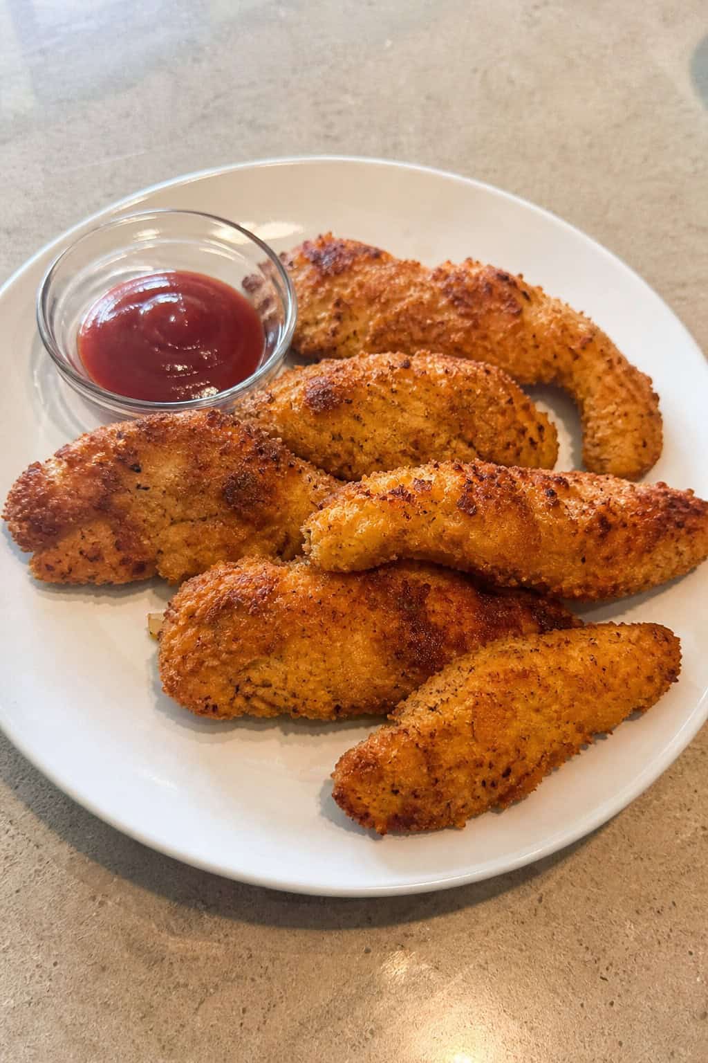Close-up of crispy apple-cider brined chicken tenders on a wooden board with dipping sauces and fresh apples in the background.