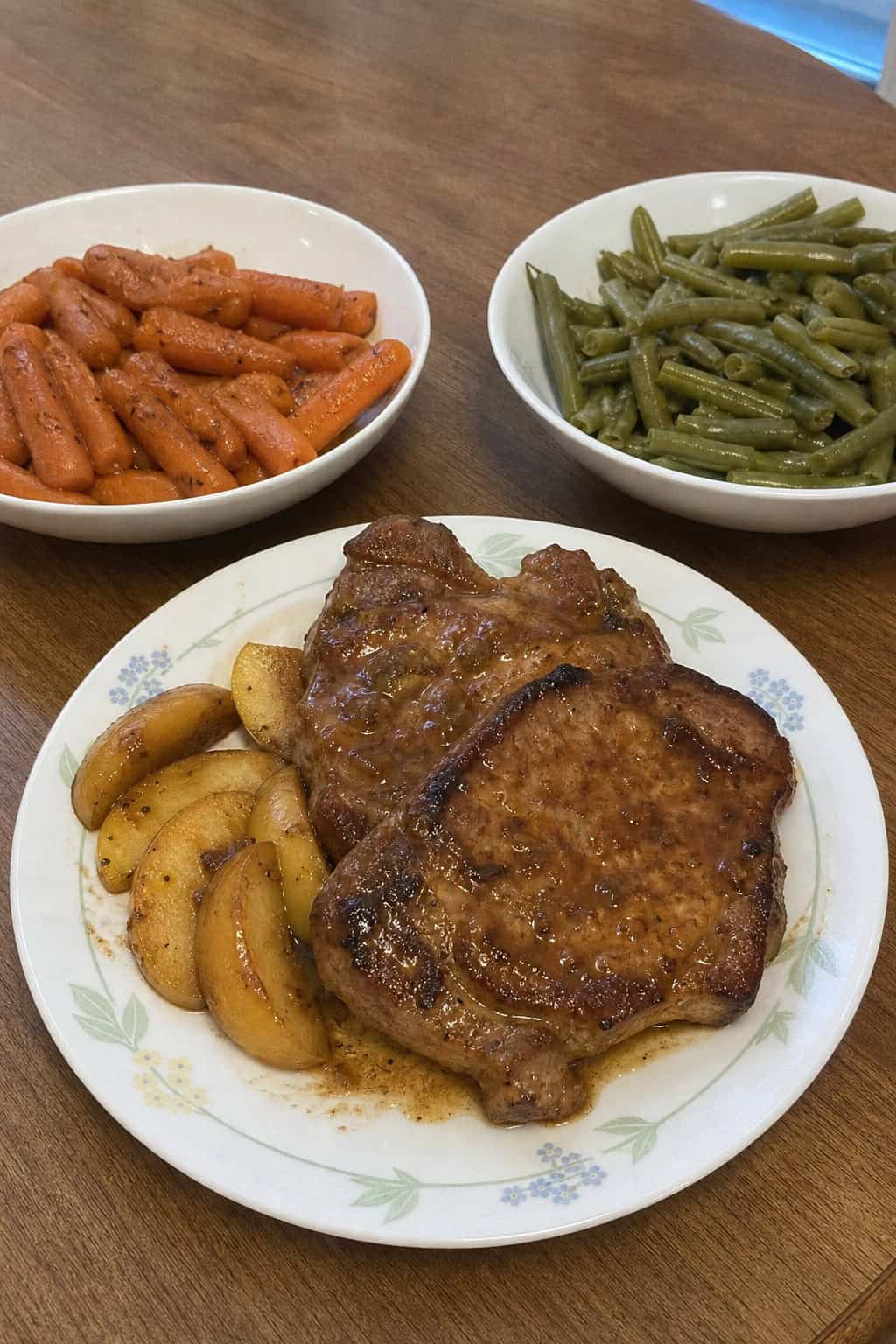 Plate of apple cider pork chops with roasted vegetables on a wooden table in a cozy kitchen setting.