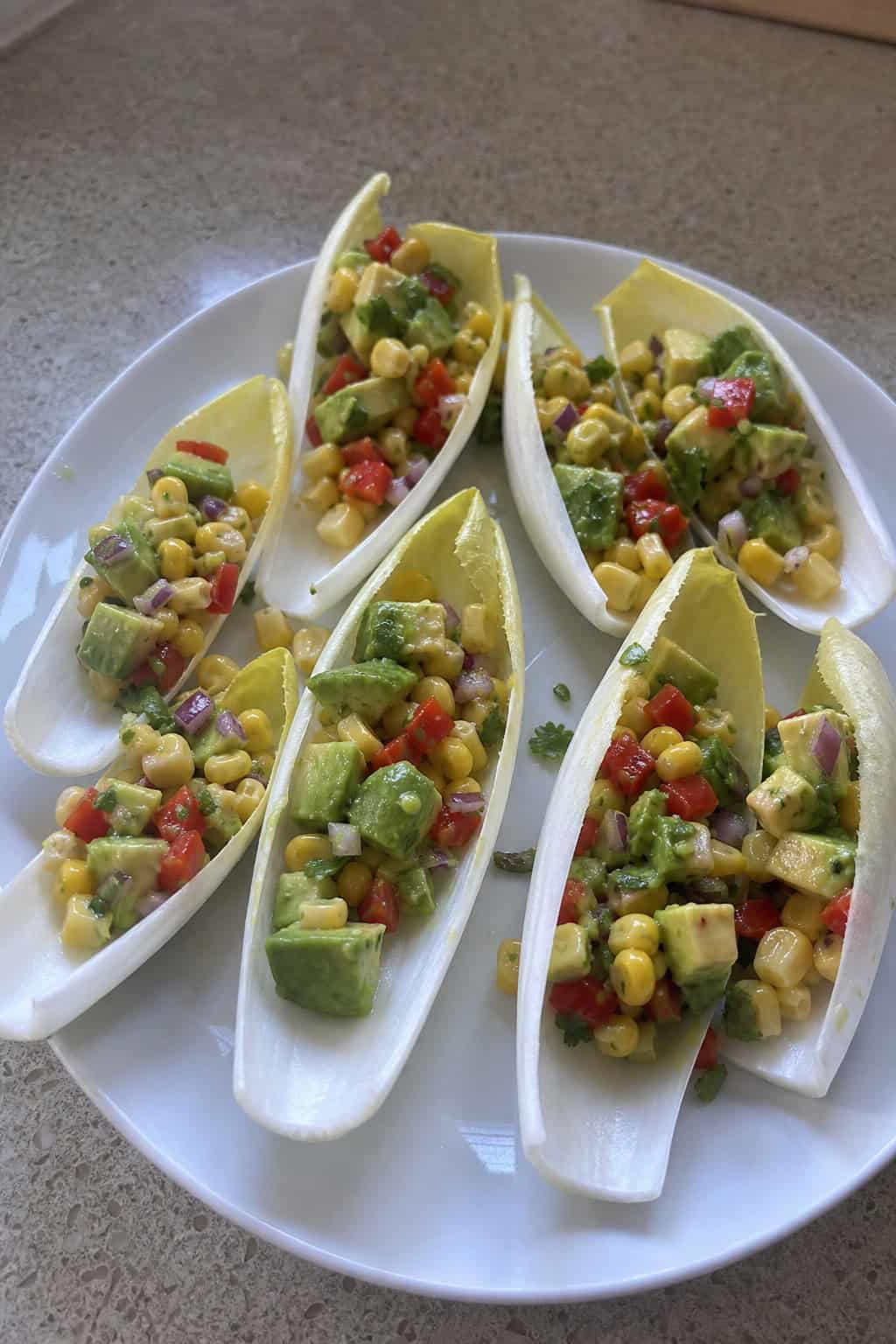 Endive spears filled with avocado corn salsa arranged on a wooden board.