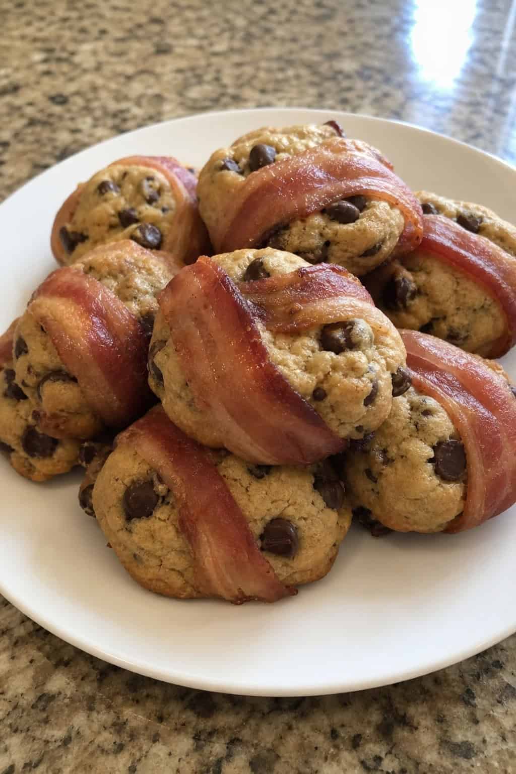 A close-up of bacon-wrapped chocolate chip cookies on a wooden board with melted chocolate chips and crispy bacon strips.