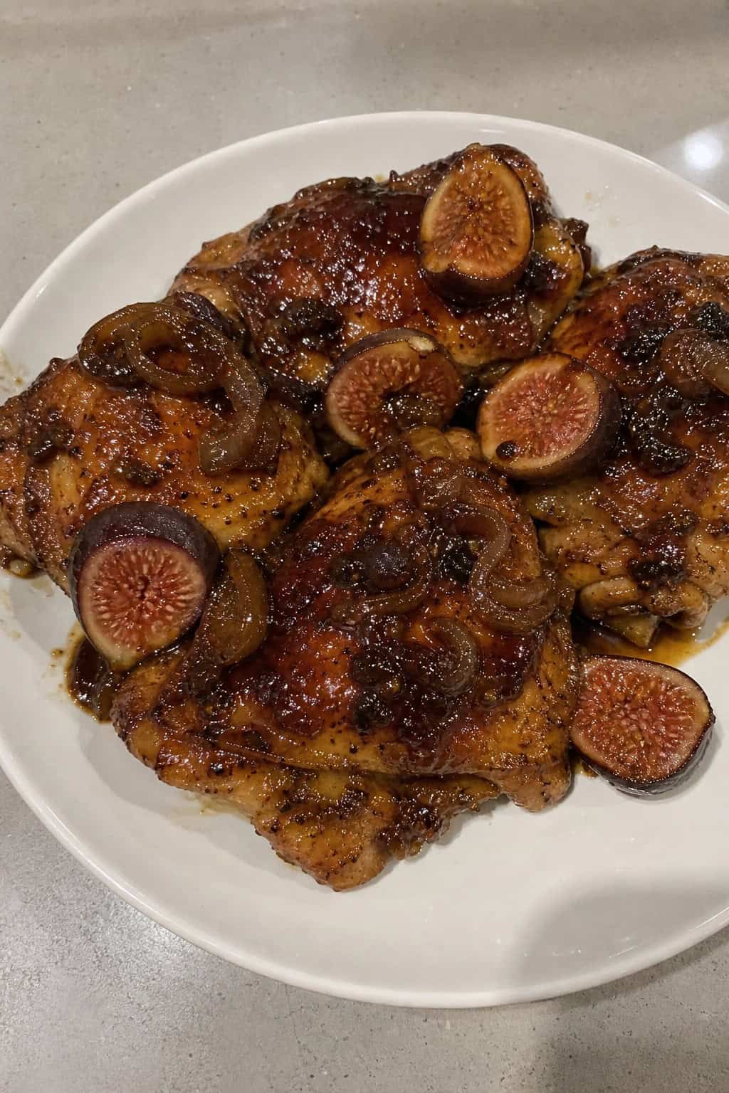 A plate of balsamic fig and shallot chicken thighs garnished with fresh herbs on a wooden table.