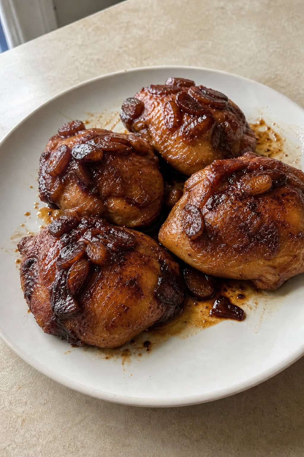 Balsamic glazed chicken thighs on a plate with a dark, syrupy glaze and soft caramelized shallot pieces, garnished with chopped fresh herbs.