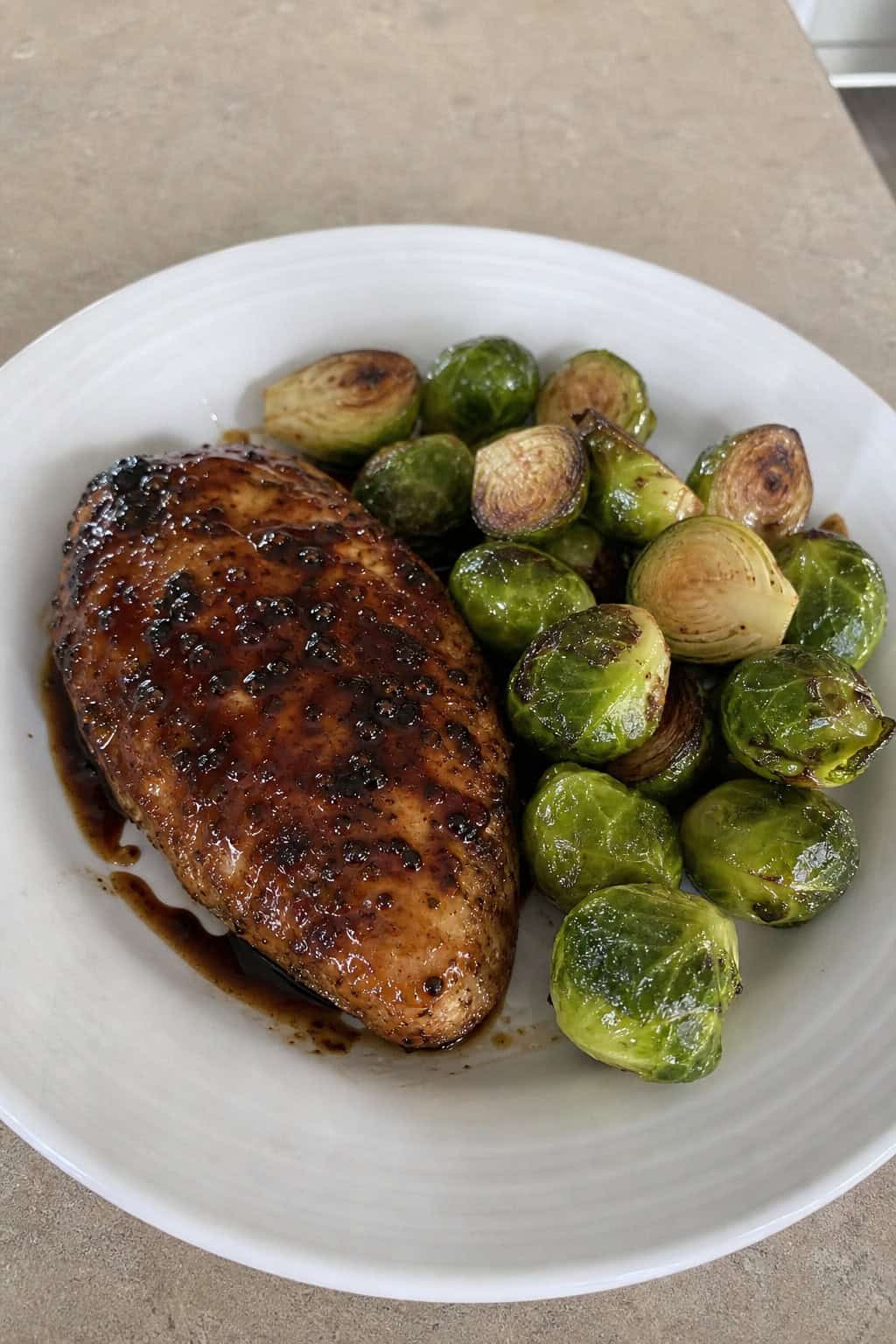 A plate with balsamic-glazed chicken breast and roasted Brussels sprouts on a wooden table.