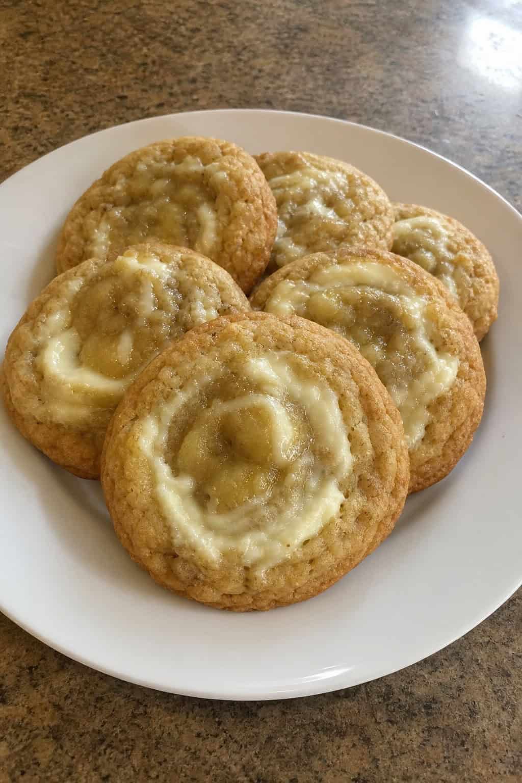 A close-up of freshly baked banana cream cheese swirl cookies on a wooden board with ripe bananas and cream cheese nearby.