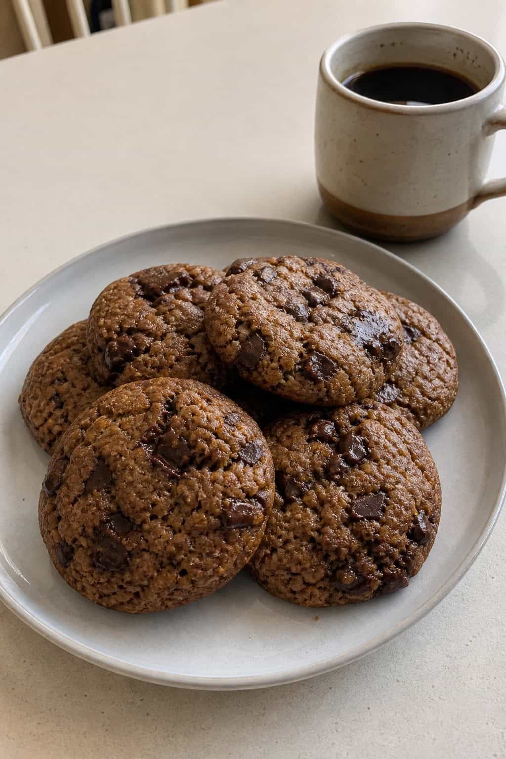 Close-up of banana dark chocolate espresso cookies on a wooden board with bananas, coffee beans, and pieces of dark chocolate nearby.
