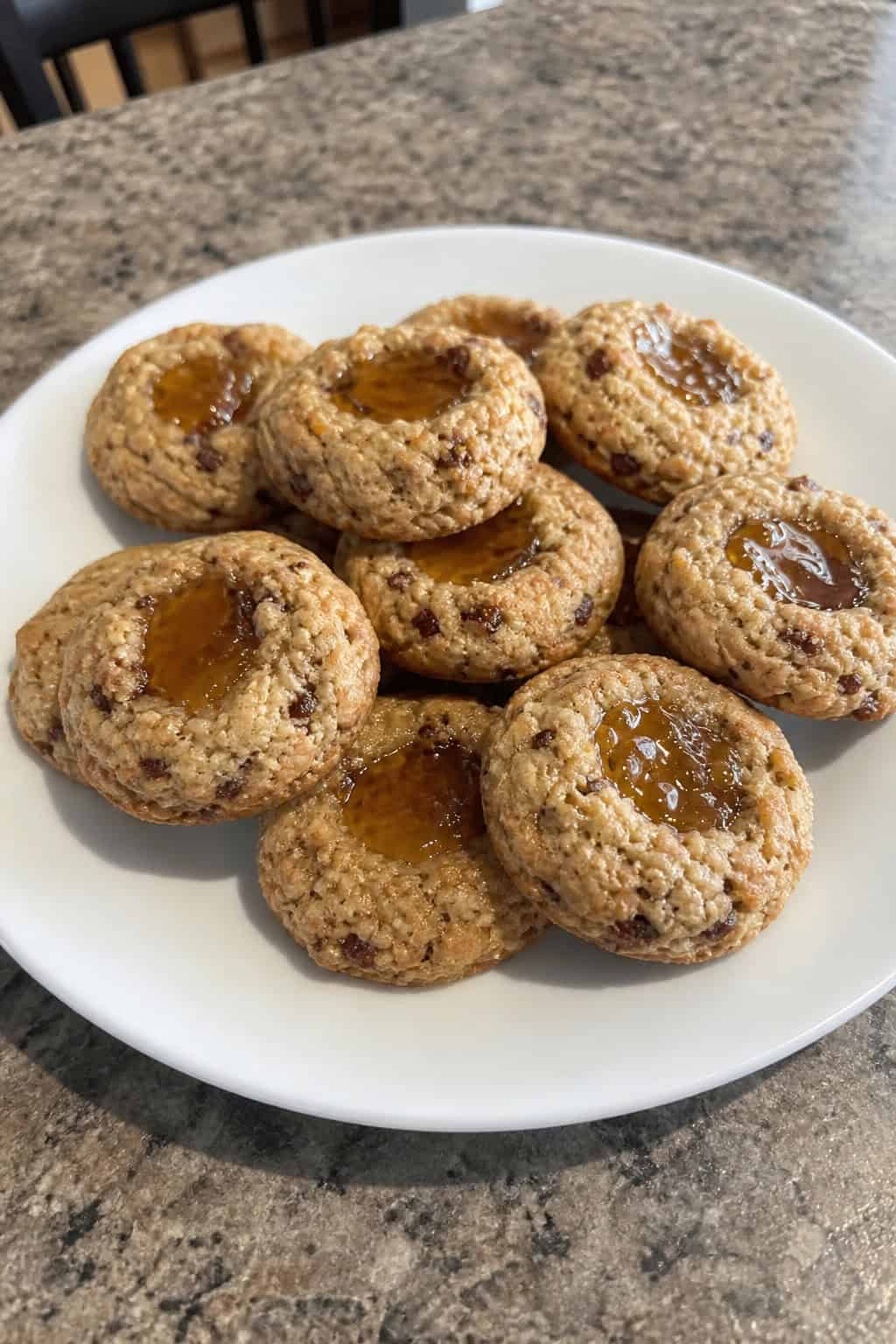 A plate of banana fig and honey thumbprint cookies surrounded by fresh bananas, figs, and a jar of honey on a wooden table.