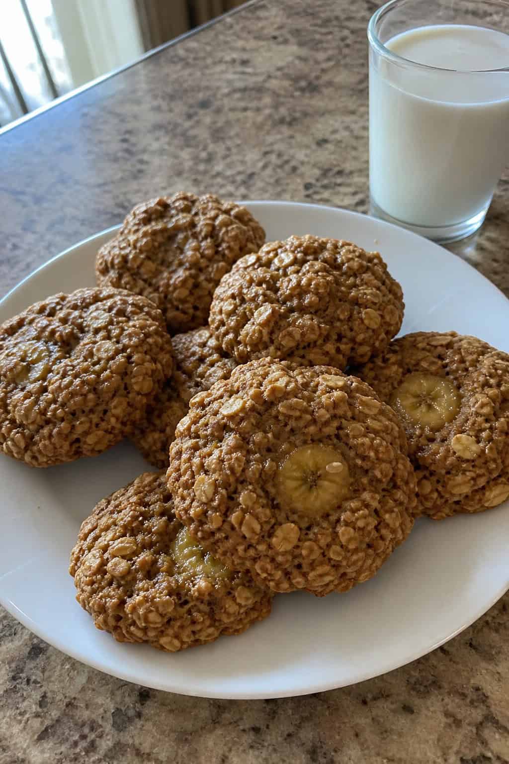 Close-up of banana oat breakfast cookies on a wooden board surrounded by bananas, oats, honey, and a glass of milk.