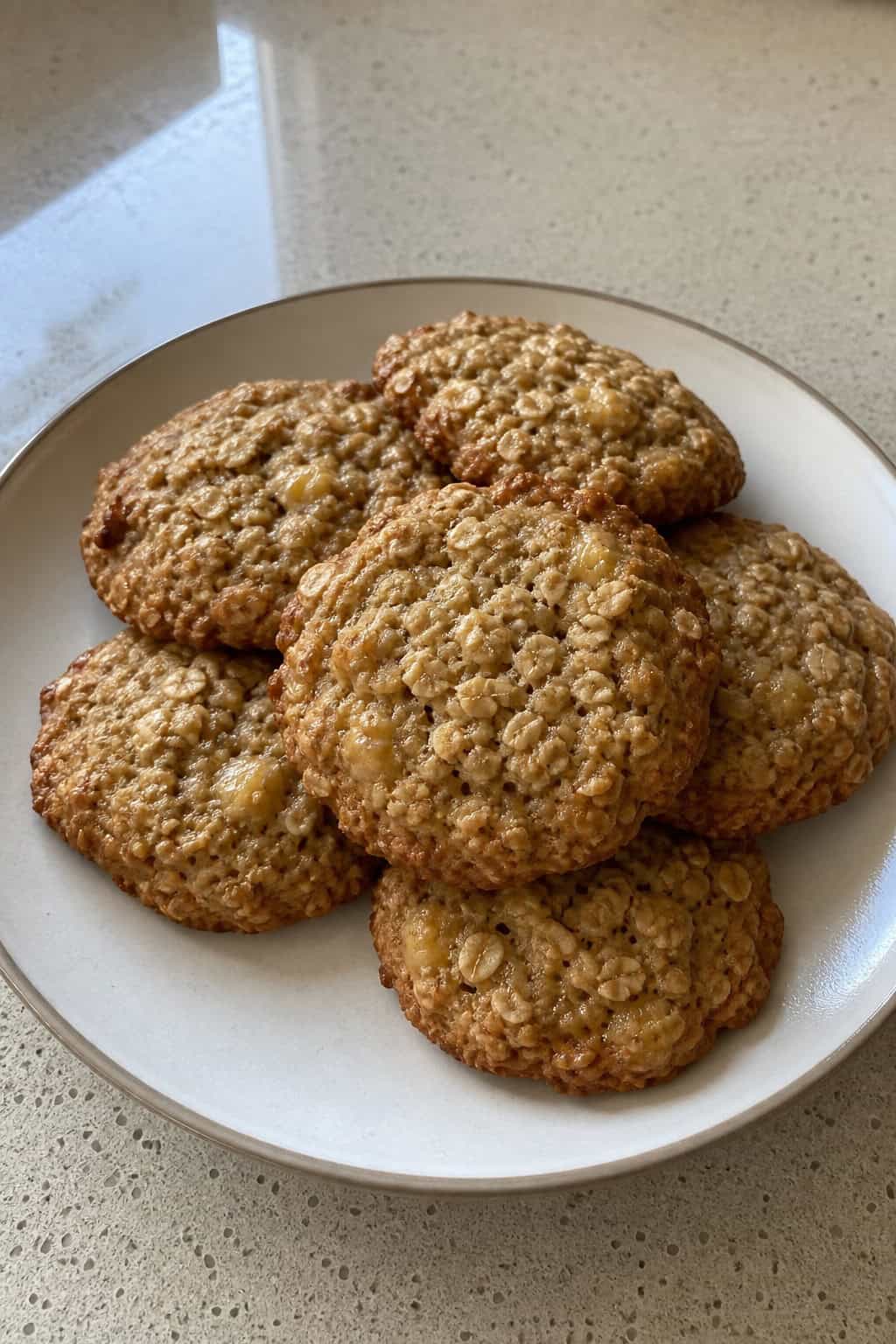 A plate of freshly baked banana oat cookies with bananas and oats nearby on a wooden surface.