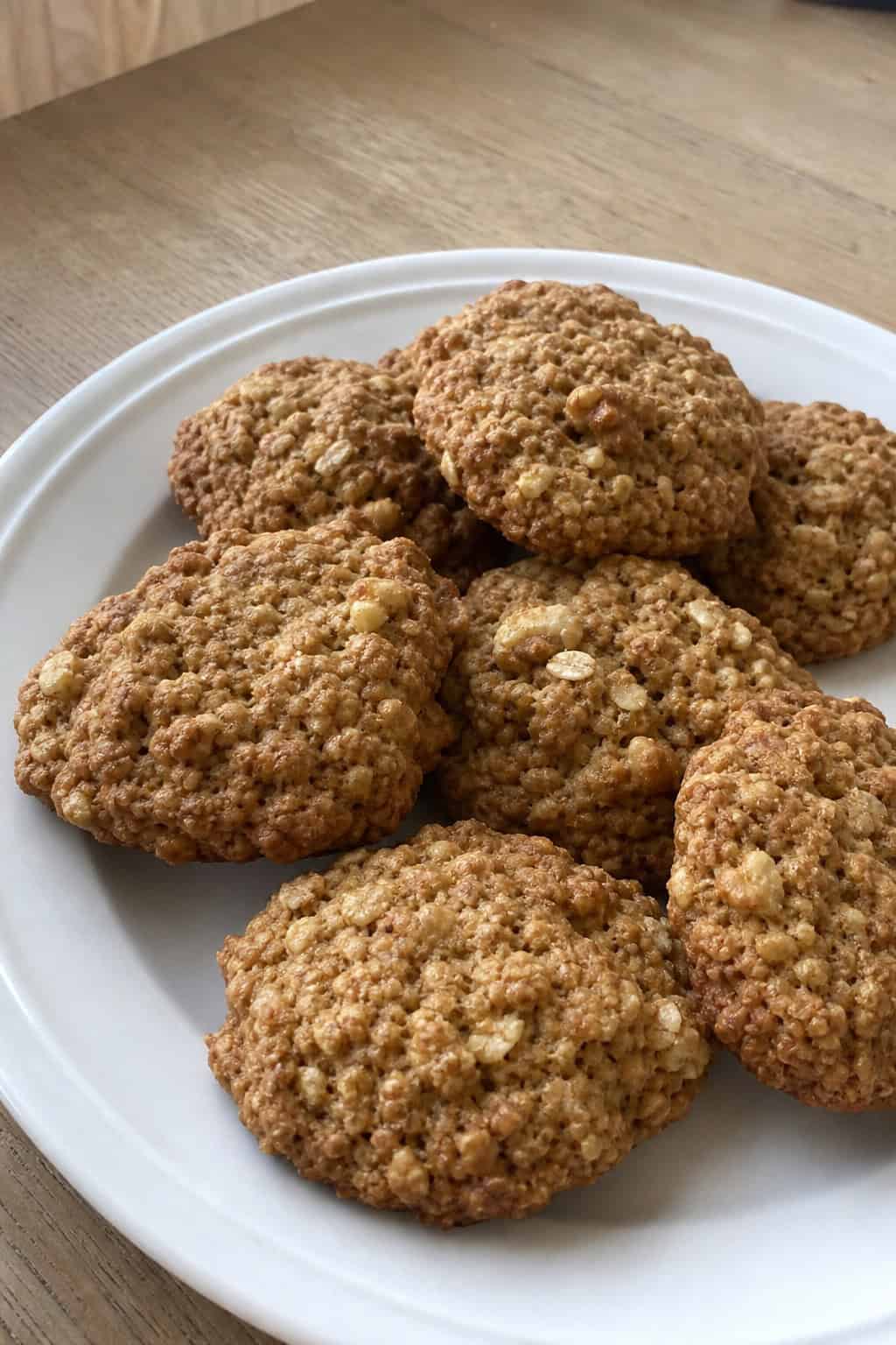 A plate of banana oatmeal breakfast cookies with walnuts on a wooden table, surrounded by bananas, walnuts, and oats.
