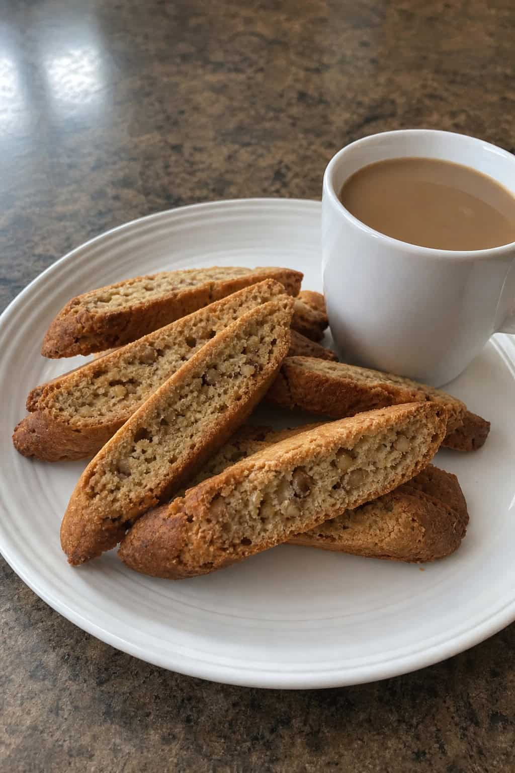 Close-up of banana walnut biscotti on a wooden board with a cup of coffee and bananas in the background.