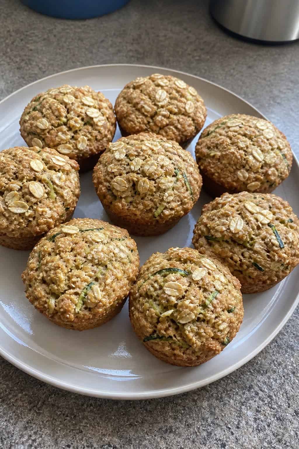 Freshly baked banana zucchini breakfast cookie muffins on a wooden table with bananas and shredded zucchini nearby.