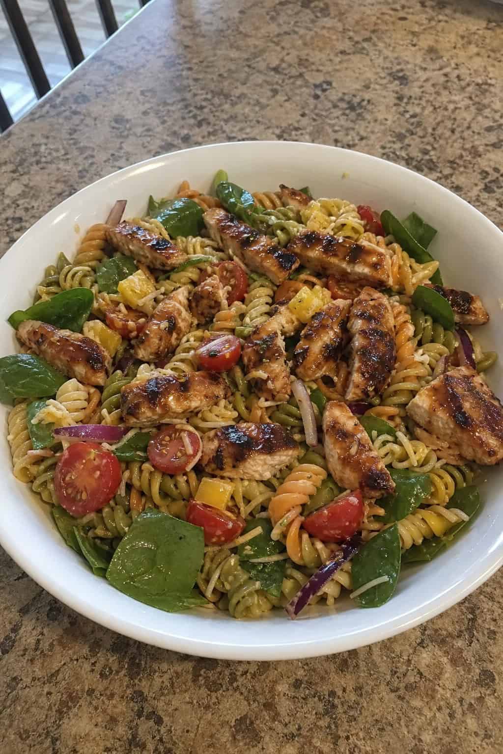 A bowl of barbecue chicken pasta salad with colorful vegetables on a wooden table.