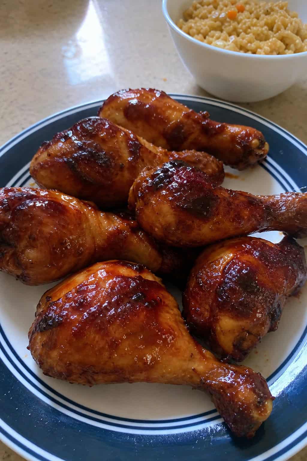 Close-up of deeply caramelized BBQ brown sugar chicken drumsticks stacked on a wood cutting board with a fresh herb garnish.