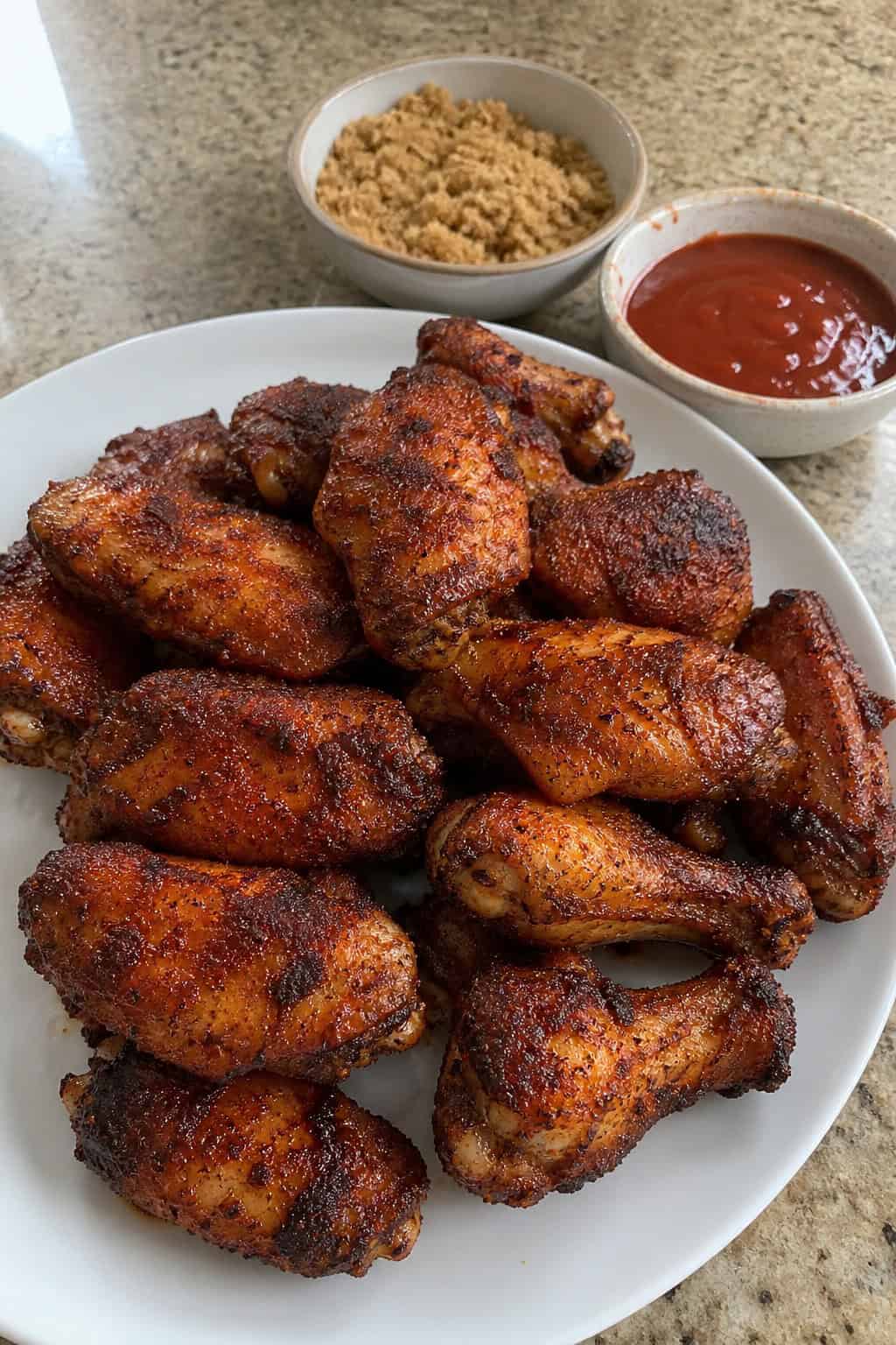 A plate of crispy BBQ dry-rub chicken wings seasoned with brown sugar and smoked paprika on a wooden board with small bowls of spices nearby.