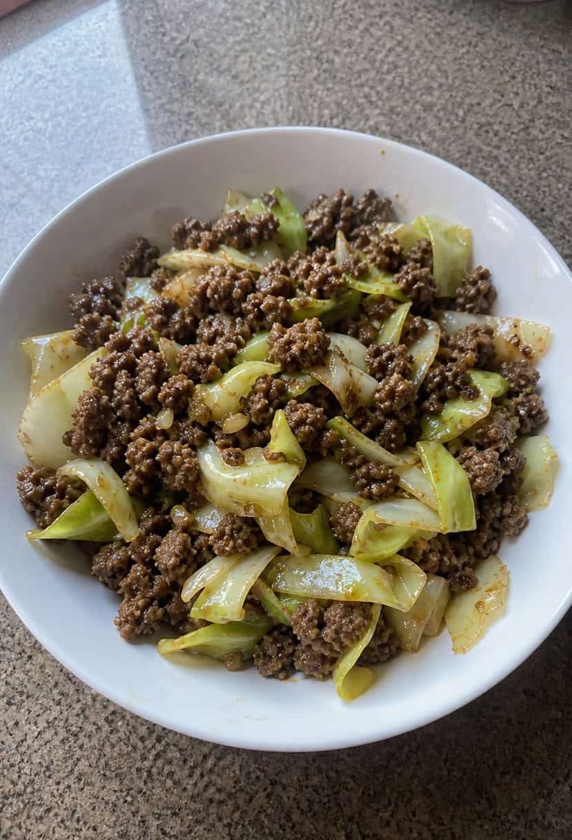 A sizzling skillet filled with ground beef, cabbage, and savory spices cooking over a hot stove