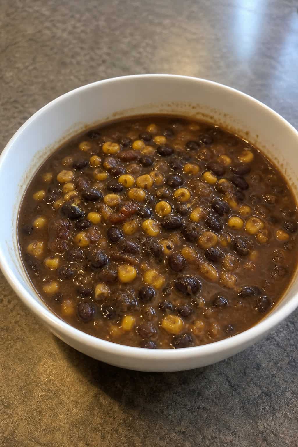 A bowl of black bean and sweet corn soup topped with fresh cilantro on a wooden table with a spoon and napkin nearby.