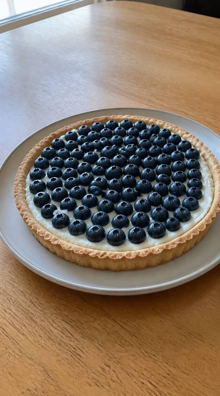 A blueberry Greek yogurt tart on a wooden table, topped with fresh blueberries and a golden crust.