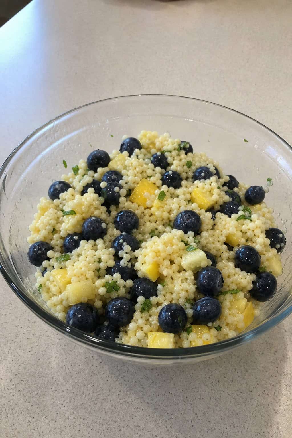 A bowl of blueberry lemon couscous salad with fresh blueberries and lemon slices on a wooden table.