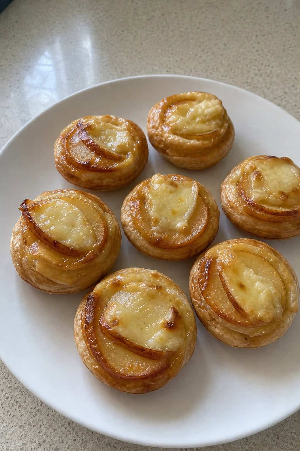 Close-up of bite-sized Brie and apple puff pastry appetizers on a wooden board with herbs around them.