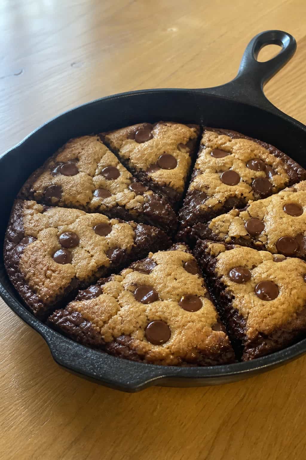 A cast iron skillet filled with a freshly baked brookie, cut into squares, showing a brownie base topped with a chocolate chip cookie layer.