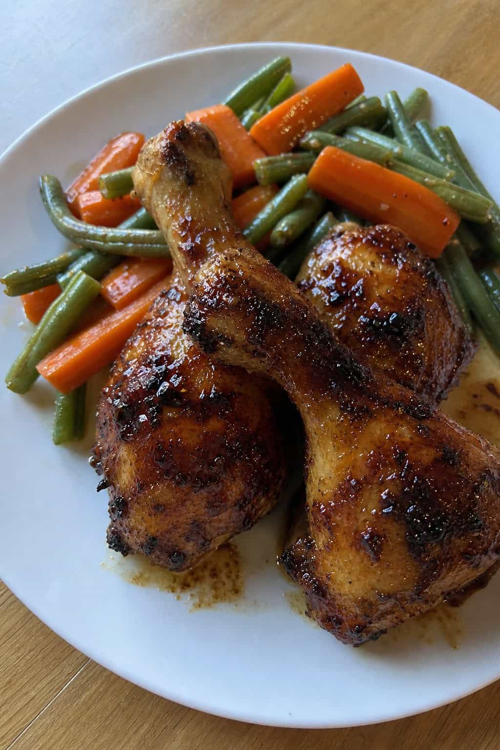 Glazed chicken legs on a white dinner plate with a deep brown caramelized coating, scattered fresh thyme sprigs, and roasted vegetables alongside.