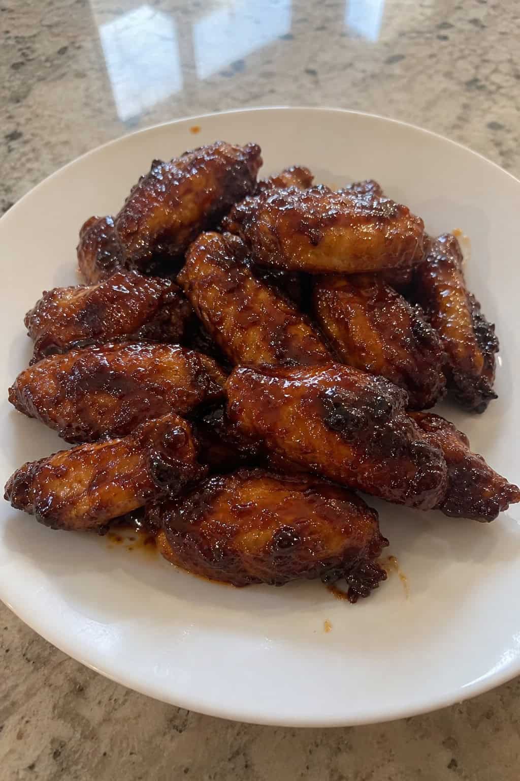 A plate of brown sugar bourbon sticky chicken wings garnished with fresh herbs, with dipping sauces and ingredients nearby.