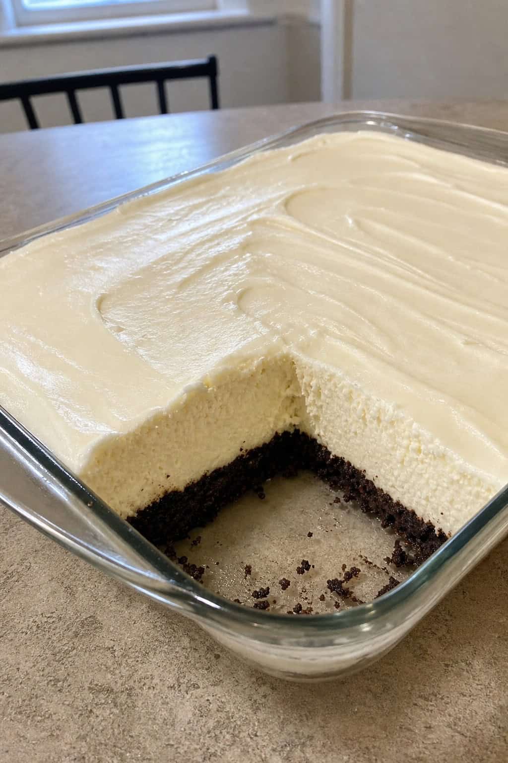 Close-up of a creamy cheesecake filling layered on a brownie crust in a dish, with fresh berries and a dessert fork nearby.
