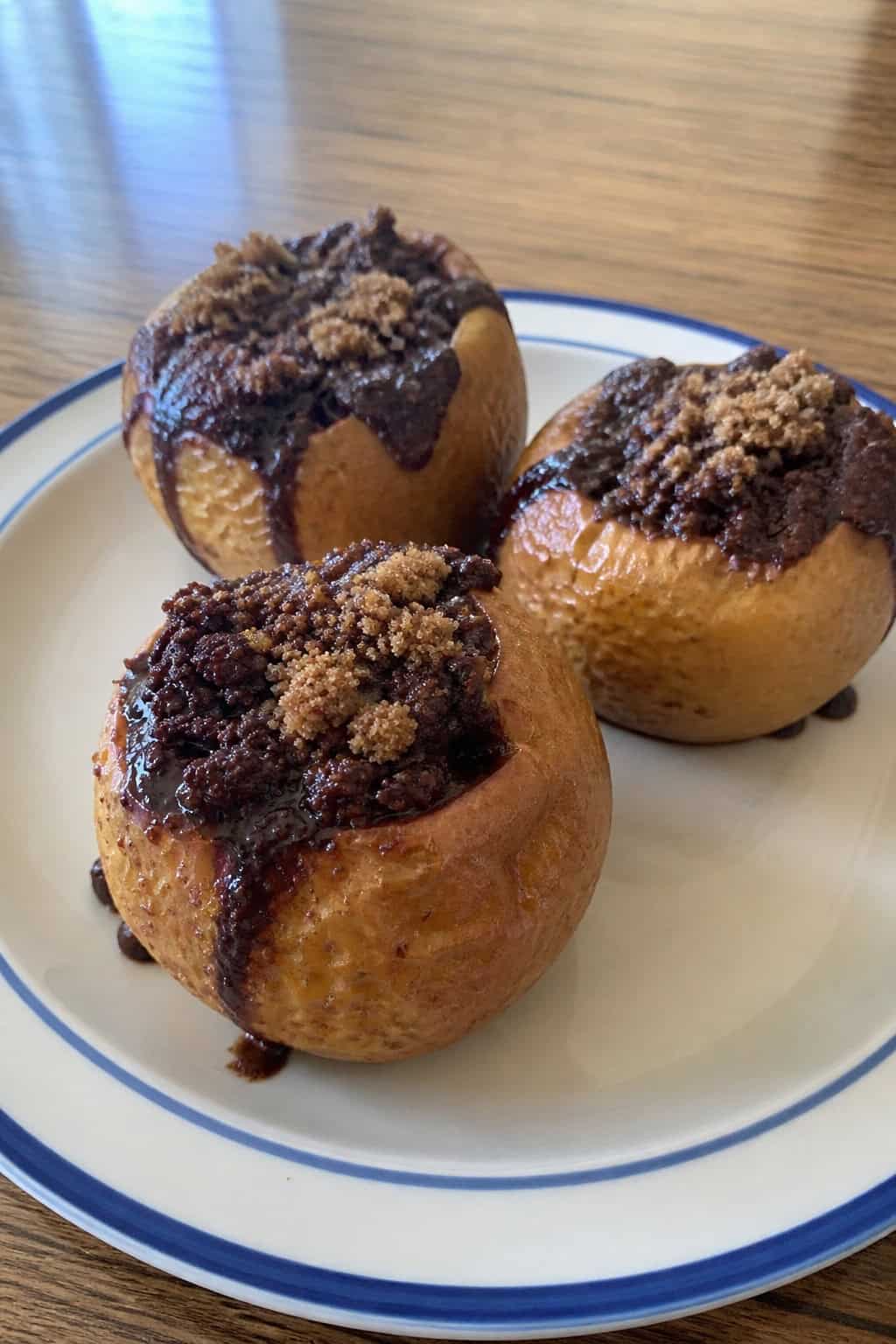 Baked apples stuffed with melted brownie filling and brown sugar on a wooden board with cinnamon sticks.